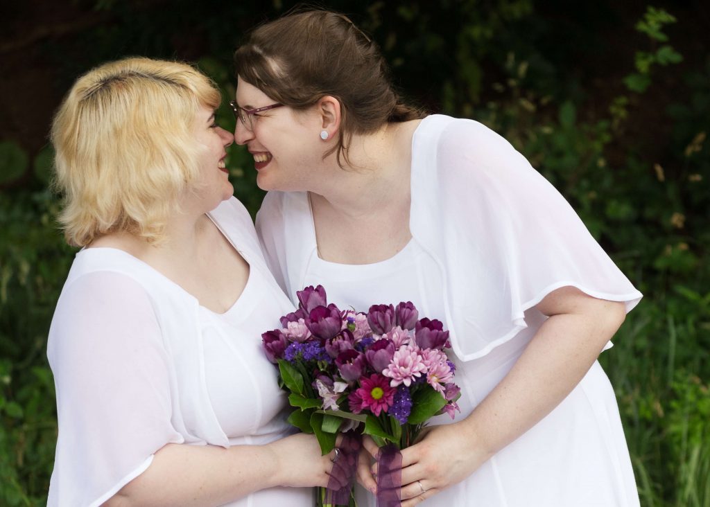 Couple holds matching purple bouquets while playfully touching noses